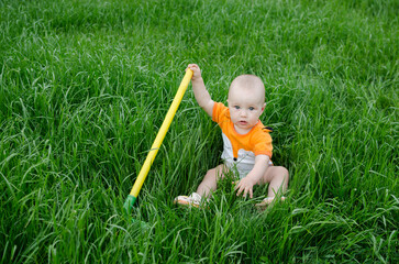  baby girl playing on green grass with rake in the summer.