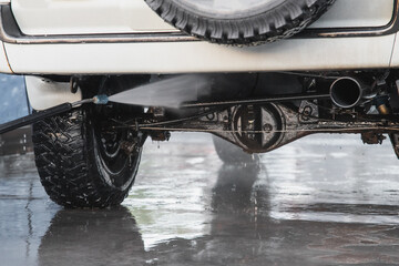 Washing the rear suspension of an SUV with a high-pressure water jet at a self-service car wash.