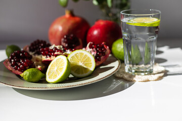 classic still life. ripe pomegranates and lime lie on a plate next to a vase with a red rose..