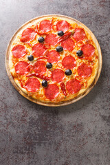 Spicy hot Diavola Pizza with sausage, mozzarella cheese, tomato sauce, chili peppers and black olives close-up on a wooden board on the table. Vertical top view from above