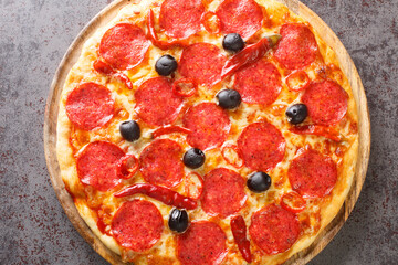 Delicious classic Pizza Devil with pepperoni sausage, cheese, tomato sauce, chili peppers and black olives close-up on a wooden board on the table. Horizontal top view from above