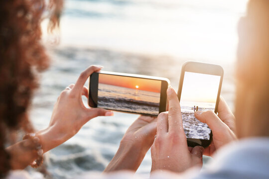 Phones, beach and couple taking a picture of the sunset while on summer vacation or weekend trip. Technology, adventure and hands of man and woman with cellphones taking photo by the ocean on holiday