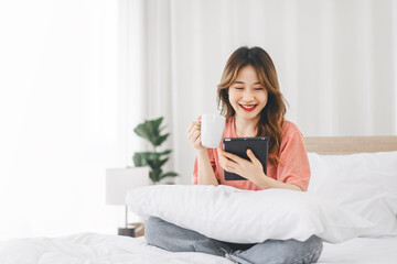 Asian woman with coffee using digital tablet for social message telemedicine and mental health or shopping online on at bedroom morning time