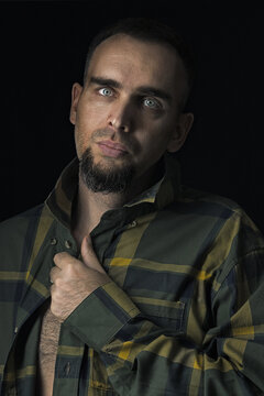 Sexy young fashionable man in an unbuttoned checked shirt against a black background. Portrait of a Caucasian man with a beard looking into the camera.