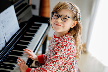 Little happy girl playing piano in living room. Cute preschool child with eye glasses having fun...