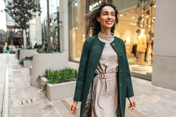 Fototapeta premium Portrait of young woman in green coat with curly hair in the city