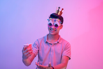 A young male celebrant points to a cup of alcohol. A partygoer lit with blue and pink neon colors.