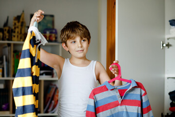 School kid boy standing by wardrobe with clothes. Child making decision for school shirt to wear....