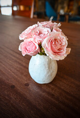 mini bouquet of pink roses in a white handmade vase on a dark wooden background