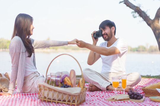 Young couple in love holding hands together and taking a photo while sit on blanket for picnic time