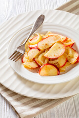 fried onion and red apple slices on white plate with fork on white wood table, vertical view from above, close-up