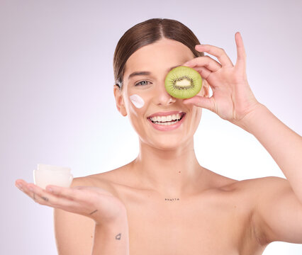 Woman, face and kiwi with moisturizer for skincare nutrition, cream or healthy diet against gray studio background. Portrait of happy female with fruit and creme for natural organic facial cosmetics
