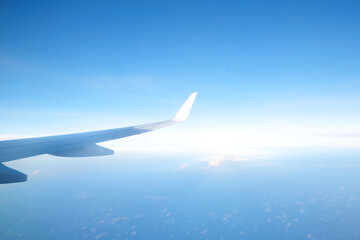 Aircraft wing flying above the beautiful clouds with sunlight in the morning. Traveling concept. Wing of an aircraft
