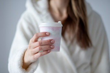 A woman holding a plastic coffee cup with a delicate watercolor drawing in her hand at home