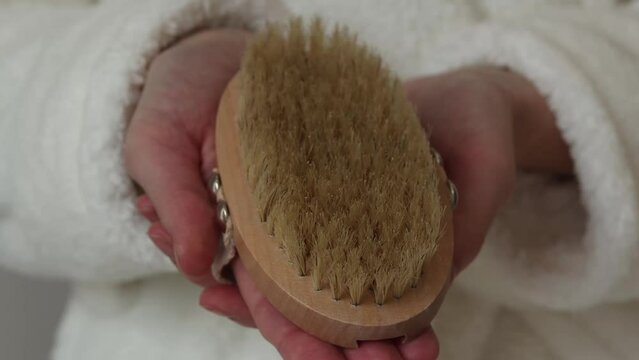 Body brush for dry massage in women's hands. Brushing body to reduce cellulite, detoxify the lymphatic system, and achieve beautiful smooth skin. Body treatment after shower