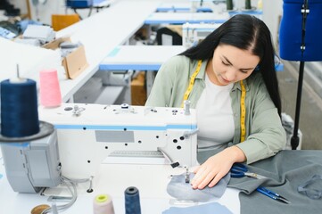 Happy attractive young woman seamstress sitting and sews on sewing machine in studio