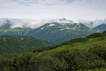 Summer mountain landscape. View of the mountain peaks. Low clouds. Travel, tourism and hiking on the Kamchatka Peninsula. Beautiful nature of Siberia and the Russian Far East. Kamchatka Krai, Russia.