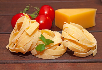 Dry nest pasta on a wooden table with tomatoes and cheese