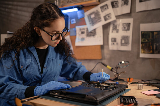 Female engineer fixing broken computer motherboard in workshop. Laptop disassembling with screwdriver at old repair shop. Electronic renovation, technology development