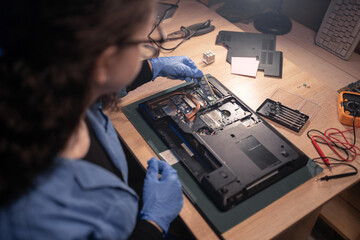 Repairman girl disassembling laptop motherboard and install memory chip. Engineer fixing broken computer at work in old repair shop. Electronic repair shop, technology renovation, business