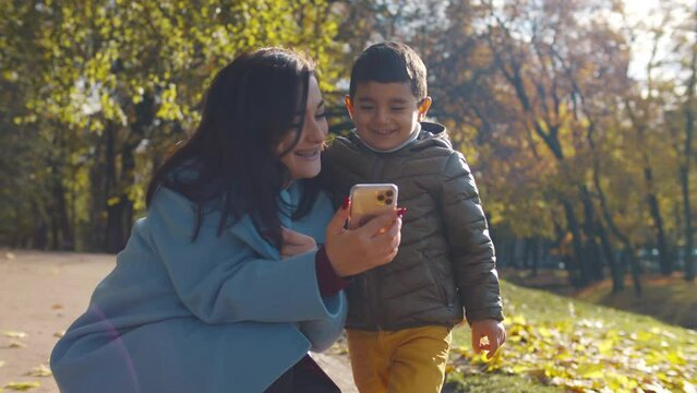 Young mother and kid look smartphone happily at park. Realtime