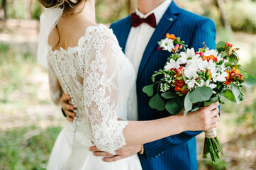 Bride holds a wedding bouquet. Wedding dress, wedding details. Groom hugs bride. Love.