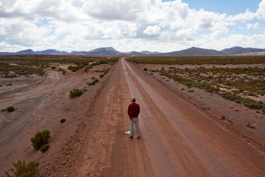 A man urinates on a lonely dirt road.