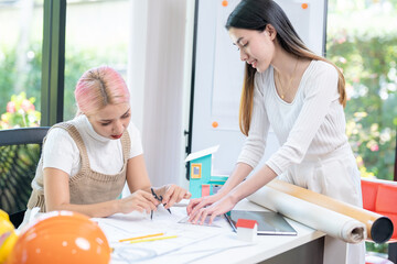 Concept of engineering consulting, Two female engineers discussing about model of building together; Two female architects are studying blueprint of building house.