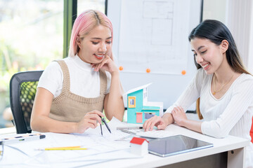 Fototapeta premium Concept of engineering consulting, Two female engineers discussing about model of building together; Two female architects are studying blueprint of building house.