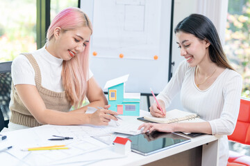 Fototapeta premium Concept of engineering consulting, Two female engineers discussing about model of building together; Two female architects are studying blueprint of building house.