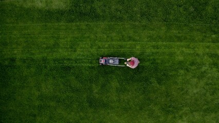 Top view of man mowing green grass in modern garden with lawn mower. Copy space