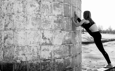 Flexible Female stretches against a silo in her yoga outfit