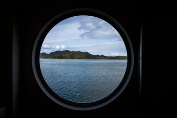 Oceanic Water And Small Forested Island Is Seen Through A Round Portal Of A Ship