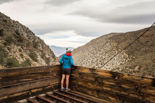SURPRISE CANYON, DEATH VALLEY, CA, USA. A young woman stands on an old wooden mining platform looking into a barren desert valley.