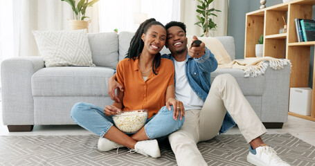 Happy black couple, eating popcorn and a movie playing in the living room of their home or house....