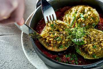 Baked and stuffed eggplants are cut with a knife and fork. Concrete background. Vegetarian dish