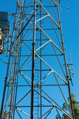 Radio or internet tower in industrial area with satelite dishes and triangular metal facets in shade with blue sky
