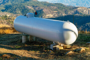 Metal round propane or natural gas tank in afternoon sun and shade on top of mountain or summit with rolling hills