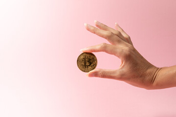cryptocurrency, finance and business concept - close up of female hand holding golden bitcoin over pink background