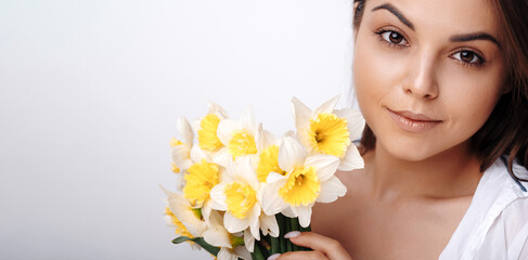 Tender millennial lady holding bunch of daffodils over grey studio background