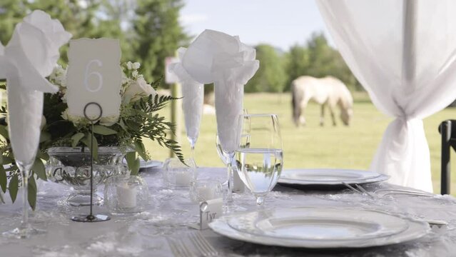 Banquet table for a wedding on a farm. Much luxury and opulence. It is day. There are horses in the background.