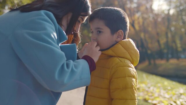 Mother zip jacket of little son in park. Realtime