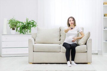 Obraz premium Pregnant woman facial expression sitting on sofa with remote control.