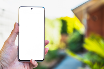 hand holding smartphone with copy space in front of stylish backyard and house exterior background, shot at shallow depth of field