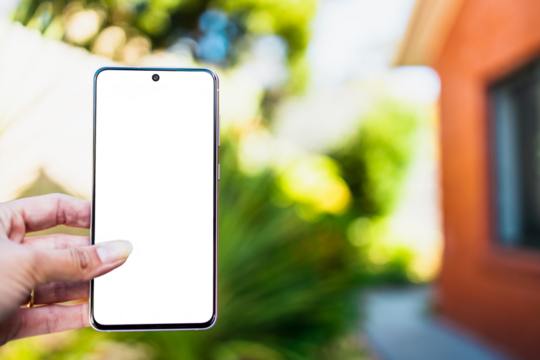 hand holding smartphone with copy space in front of stylish backyard and house exterior background, shot at shallow depth of field
