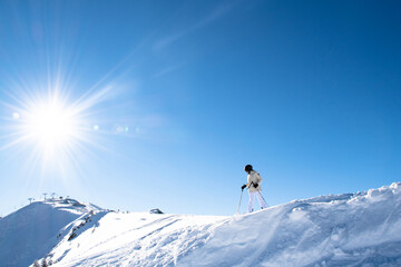 Fototapeta na wymiar Skier on the mountain looking at the landscape with bright sun enjoying the snow and the ski resort. Doing sports outdoors. Lifestyle