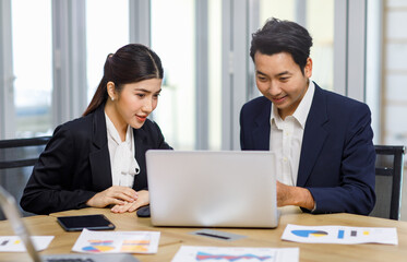 Millennial Asian professional successful male businessman manager mentor helping coaching advising new female businesswoman employee staff in formal business suit sitting working with laptop computer