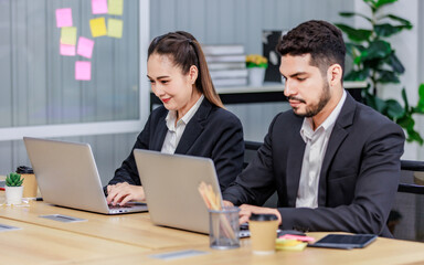 Millennial Asian Indian professional bearded male businessman female businesswoman employee staff in formal business suit sitting working typing laptop notebook computer in company office workplace