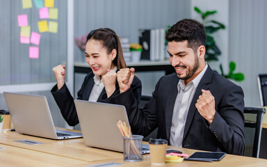 Fototapeta na wymiar Millennial Asian Indian professional successful bearded male businessman and female businesswoman employee colleague in formal business suit sitting holding fists up celebrating job deal achievement