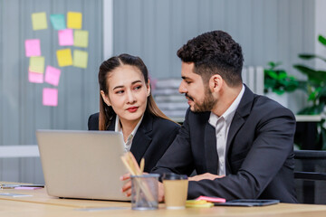 Millennial Asian Indian professional bearded male businessman female businesswoman employee staff in formal business suit sitting working typing laptop notebook computer in company office workplace